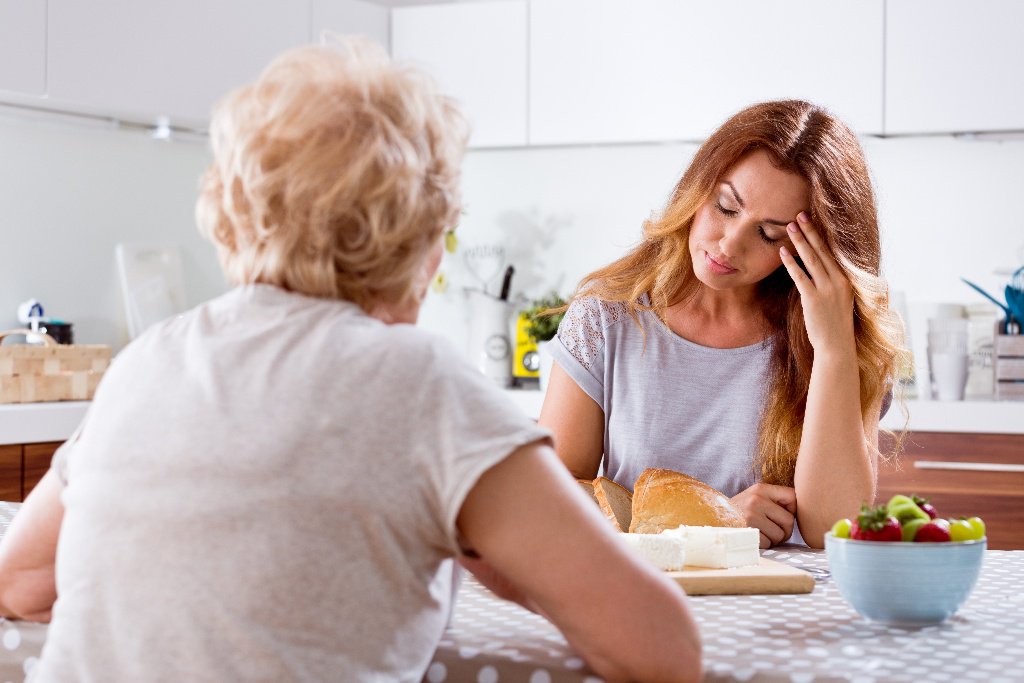 A female caregiver looking tired while talking to a senior woman.