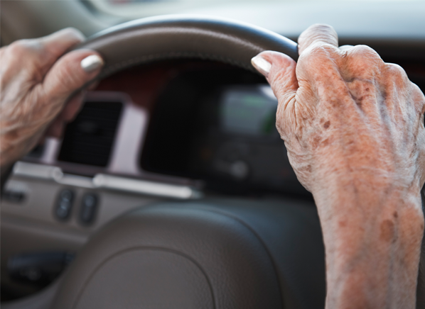 A senior's hands holding a car's steering wheel.