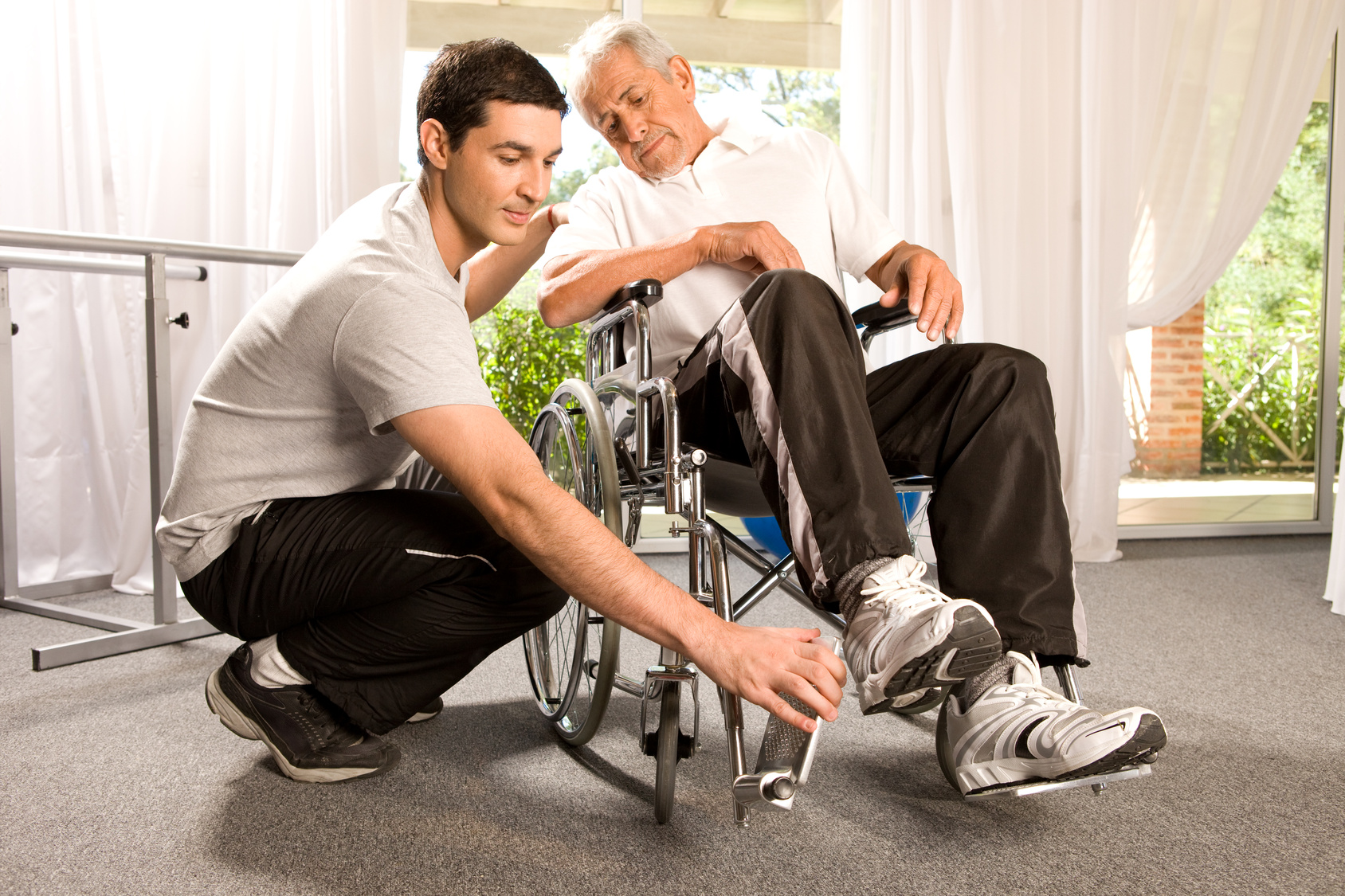 A young male caregiver helping a senior man with his wheelchair.