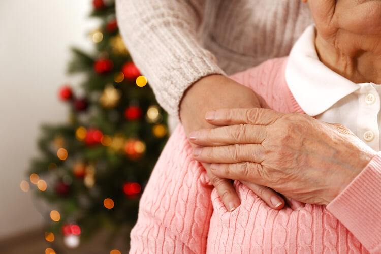 A senior woman holding the hand of a younger woman in front of a Christmas tree.