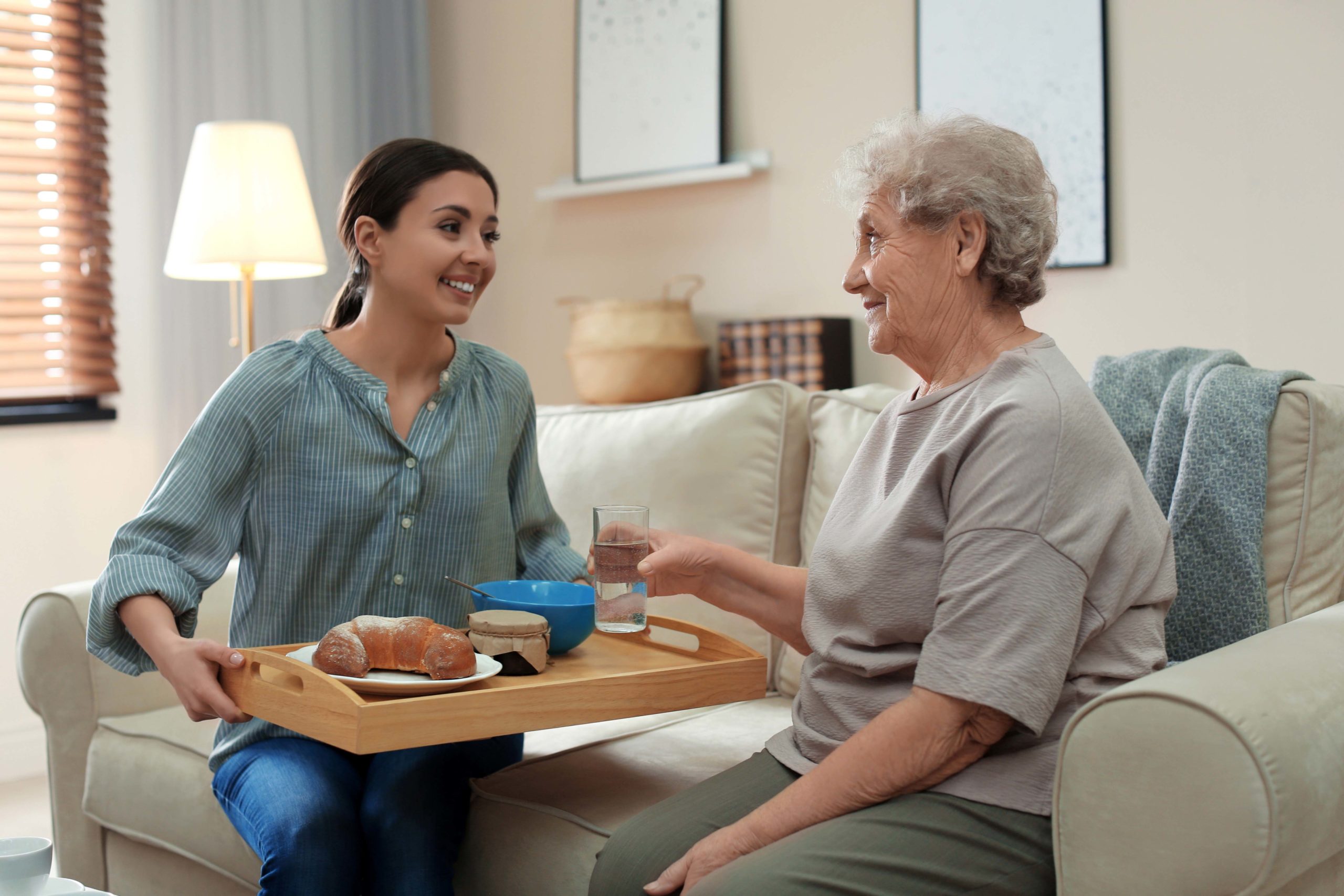 A caregiver presenting a tray of food to a senior woman.