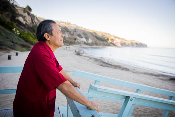 Old man watching beach from deck.