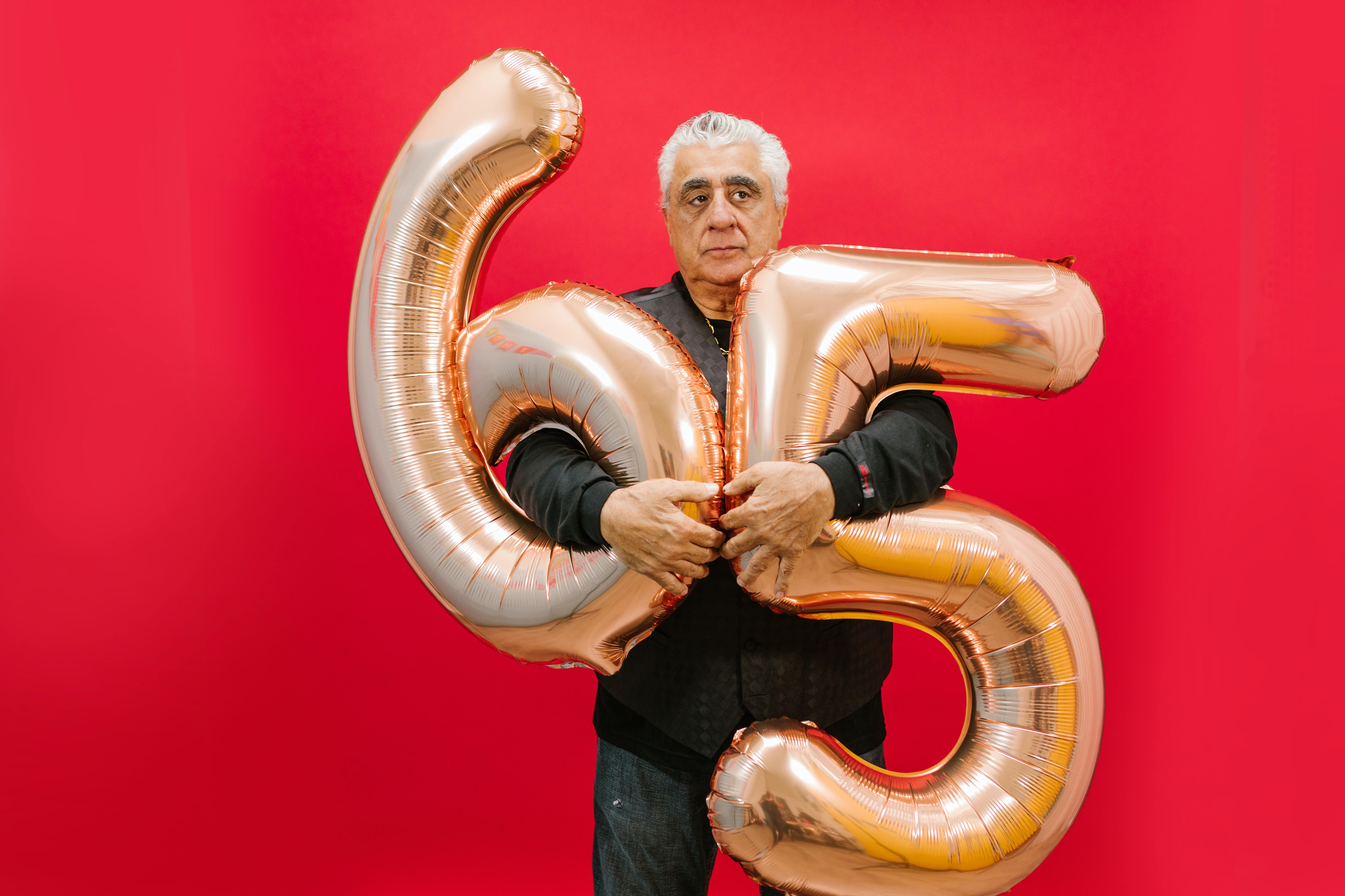 A man holding balloons that show he is 65.