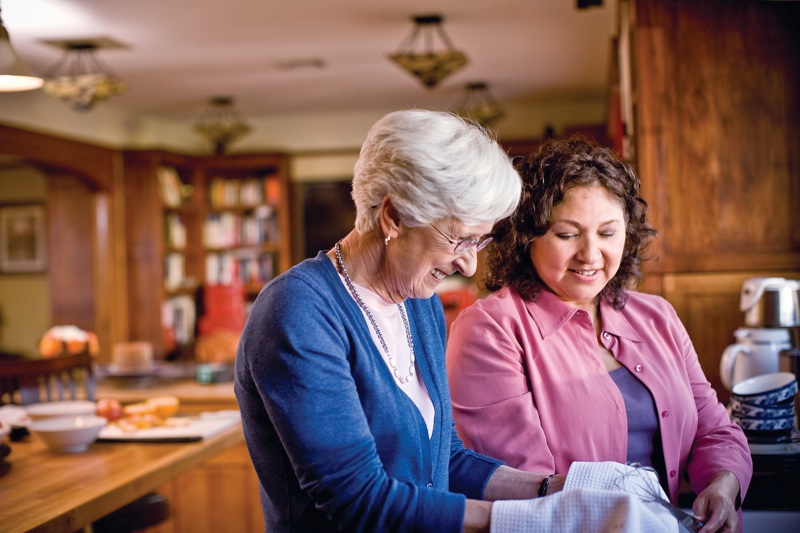 A female caregiver helping a senior woman to wash the dishes.