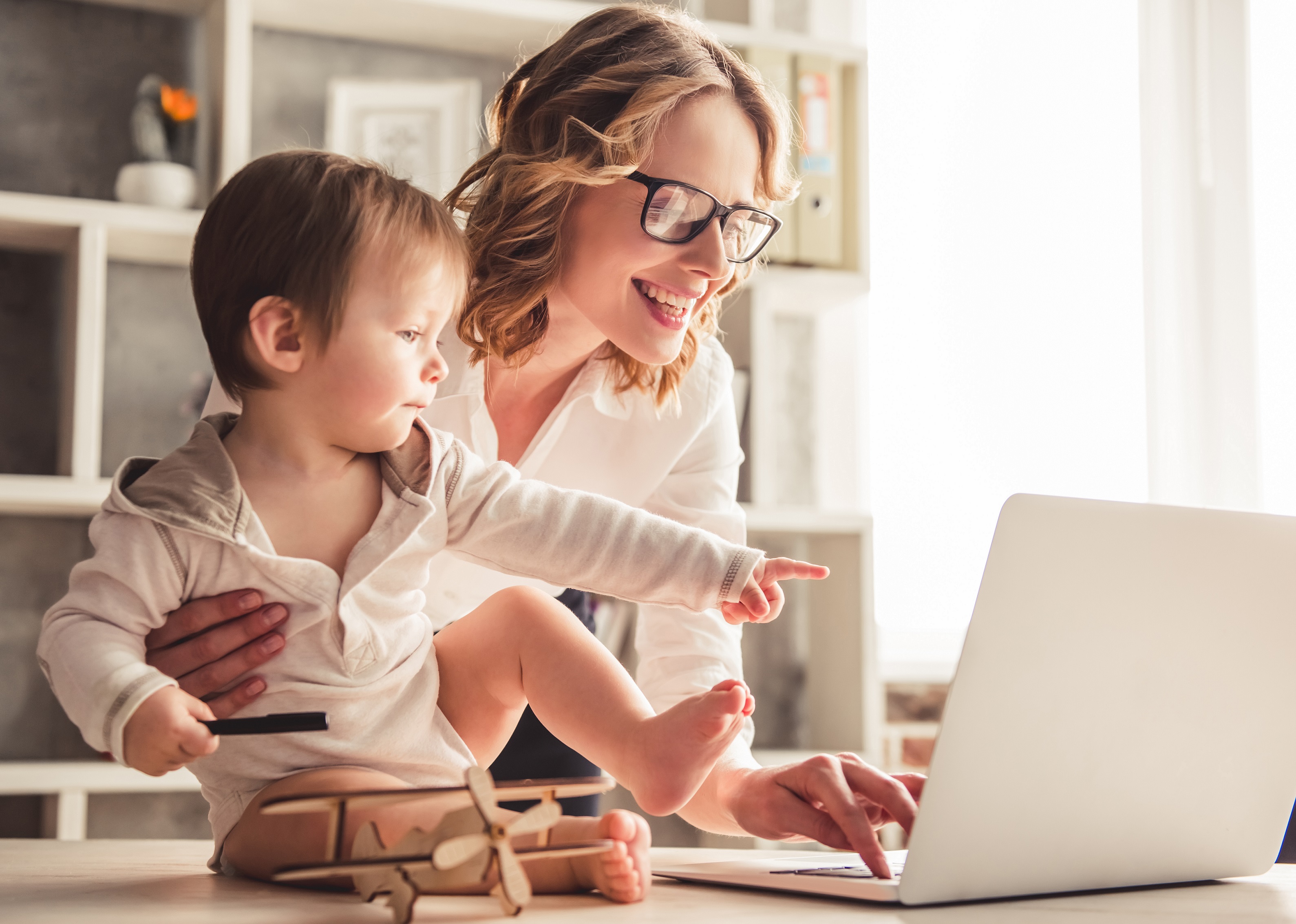 A woman at her laptop holding an infant.