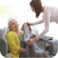 A carer providing a blanket to an elderly woman in a chair.