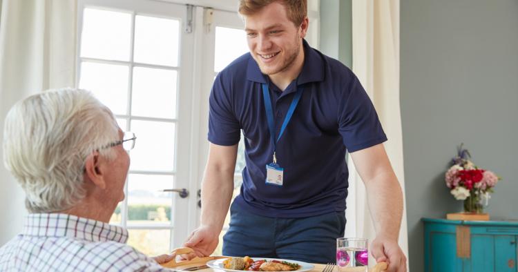 A caregiver presenting a tray of food to a man.