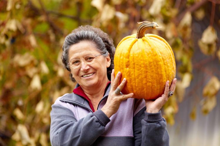 A senior woman holding a pumpkin aloft.