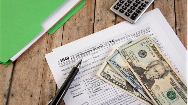 A desk with IRS forms, cash, a pen and a calculator.